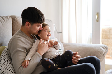 Man enjoying time with his little daughter while relaxing together on a sofa at home.