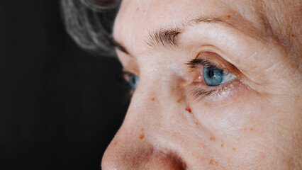 Female blue eye of mature caucasian woman, skin wrinkles, moles, real person. Side view, close-up,...