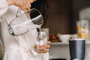 Close-up of the hands of a girl in the kitchen who pours clean water into a glass. Healthy eating