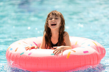 Smiling little girl swims in the sea or pool on a pink inflatable donut ring