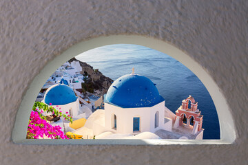 Blue domes and traditional white houses with bougainvillea flowers. Oia village, Santorini island,...