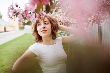 Portrait of good-looking woman among pink bokeh flowers outdoors in spring, selective focus. 