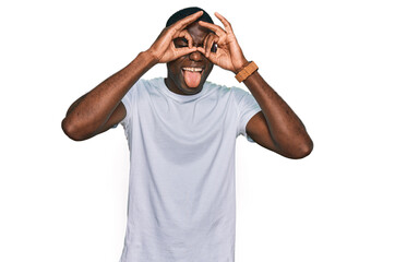 Fototapeta na wymiar Young african american man wearing casual white t shirt doing ok gesture like binoculars sticking tongue out, eyes looking through fingers. crazy expression.