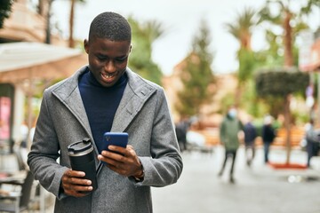Fototapeta premium Young african american man using smartphone drinking coffee at the city