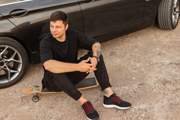 Obraz premium Hipster man sits by the car on a longboard