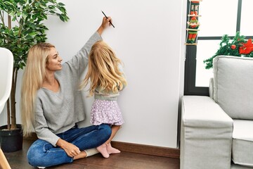 Mother and daughter measuring child height writing mark on wall at home