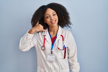 Young african american woman wearing doctor uniform and stethoscope smiling doing phone gesture with hand and fingers like talking on the telephone. communicating concepts.