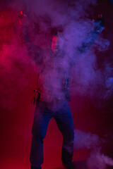 soldier in full gear with weapons. a man in headphones, body armor, with a backpack and a belt. red background. colored, blue-red light. smoke around the military. explosion, chemical attack