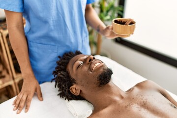 Obraz na płótnie Canvas African american man reciving facial treatment at beauty center.