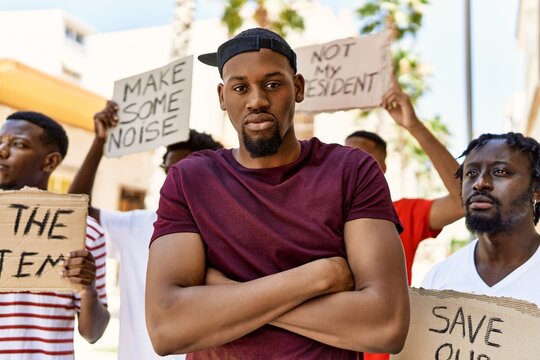Young activist man with arms crossed gesture standing with a group of protesters holding banner protesting at the city.