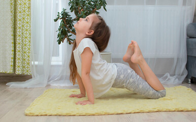 little girl does yoga and practices meditation at home in the living room. Children's yoga for...