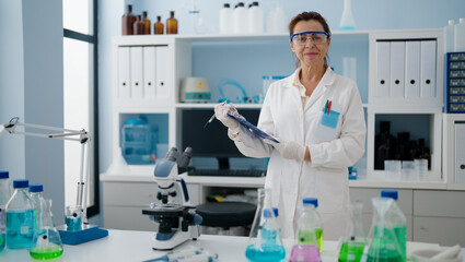 Middle age hispanic woman wearing scientist uniform holding checklist at laboratory