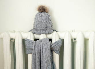 Vintage heating radiator with gray wool knitted winter hat and scarf. The electricity and gas bill...