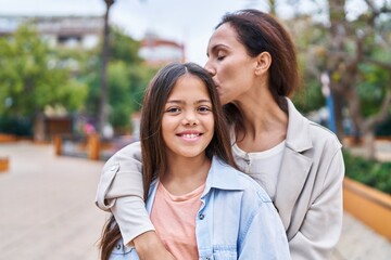 Fototapeta premium Woman and girl mother and daughter hugging each other and kissing at park