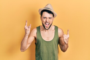Young hispanic man wearing summer hat shouting with crazy expression doing rock symbol with hands...