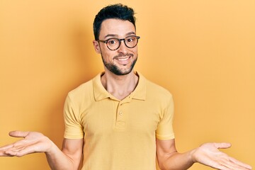 Young hispanic man wearing casual clothes and glasses clueless and confused expression with arms...