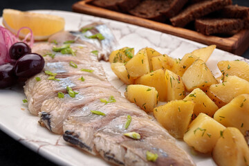 Salted herring with potatoes and toast on a dark background