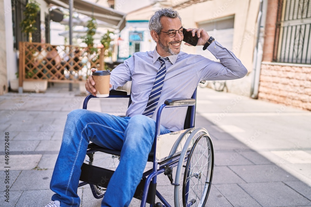 Sticker Middle age hispanic man sitting on wheelchair talking on the smartphone at street