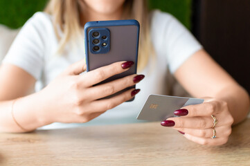 Young woman holding credit card and using smart phone at home.