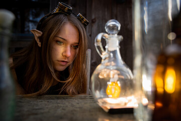 Fairy beautiful female elf with goggles on her head looking at a mysterious bottle