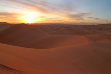 Fototapeta na wymiar Sun at horizon in the sand dunes of Erg Chebbi desert during golden hour at sunset in Morcco