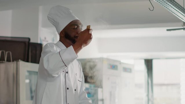 African american cook taste testing vegetable soup on stove, feleing confident about professional cuisine dish. Authentic chef cooking fresh meal and delicious food in restaurant kitchen.