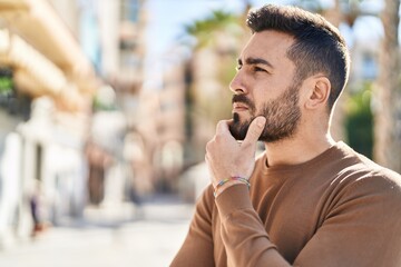 Young hispanic man standing with doubt expression at street