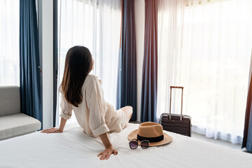 Young asian woman traveler with luggage sitting and relaxing on the bed in hotel room