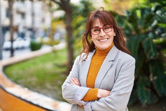Middle age woman business executive standing with arms crossed gesture at park