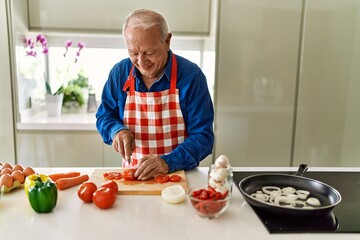 Senior man smiling confident cutting tomato at kitchen