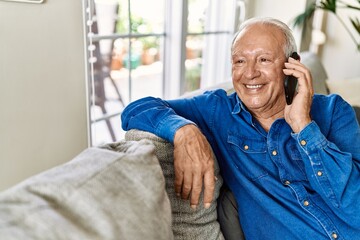 Senior man with grey hair sitting on the sofa at the living room of his house having a conversation speaking on the phone