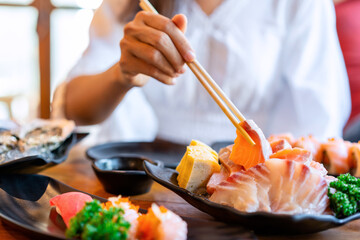Young asian woman eating sashimi set in japanese restaurant