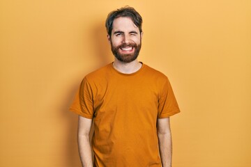 Caucasian man with beard wearing casual yellow t shirt winking looking at the camera with sexy expression, cheerful and happy face.