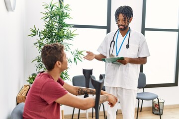 Fototapeta premium Two men physiptherapist and patient having medical consultation using crutches at hospital waiting room