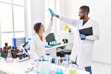 Man and woman scientist partners holding clipboard high five raised up hands at laboratory