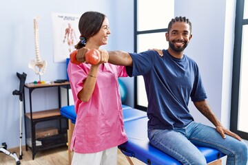 Man and woman wearing physiotherapist uniform having rehab session stretching arm holding dumbbell...