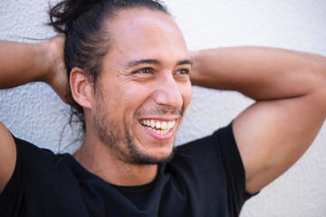 Cheerful man with pulled up hair bun and hands behind head over white background