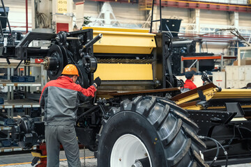 Worker assembles agricultural vehicle combine harvester in industrial factory workshop.