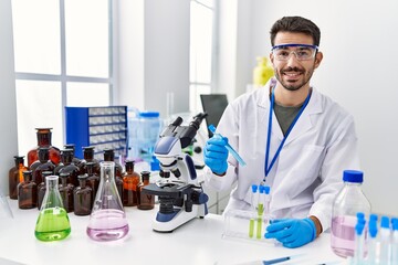 Young hispanic man wearing scientist uniform holding test tube at laboratory