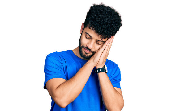 Young arab man with beard wearing casual blue t shirt sleeping tired dreaming and posing with hands together while smiling with closed eyes.