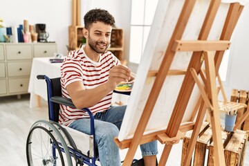 Young arab disabled artist man drawing sitting on wheelchair at art studio.