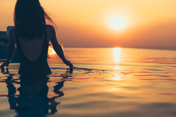 silhouette of woman in the pool water on summer vacation with sunset view.