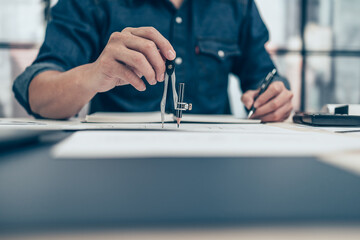 Architect using divider compass working on blueprint and make a note on book. Construction concept. Engineering tools