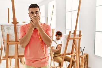 Young hispanic man at art studio shocked covering mouth with hands for mistake. secret concept.