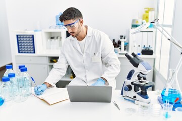 Handsome hispanic man working as scientific with microscope and laptop at laboratory