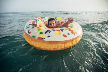 Joyful child on inflatable ring ride on breaking wave. Travel lifestyle, swimming activities. Selective focus