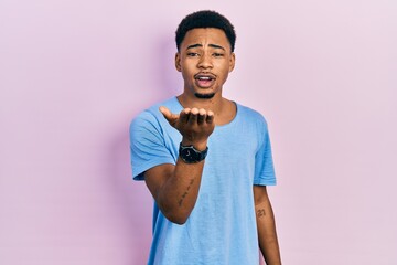 Young african american man wearing casual blue t shirt looking at the camera blowing a kiss with hand on air being lovely and sexy. love expression.