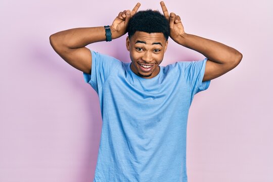 Young african american man wearing casual blue t shirt posing funny and crazy with fingers on head as bunny ears, smiling cheerful