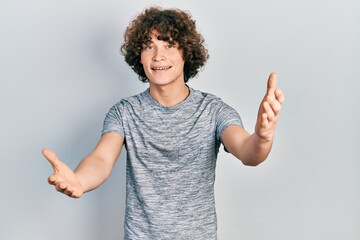 Handsome young man wearing casual grey t shirt looking at the camera smiling with open arms for hug. cheerful expression embracing happiness.