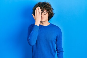 Fototapeta na wymiar Handsome young man wearing casual clothes and glasses covering one eye with hand, confident smile on face and surprise emotion.